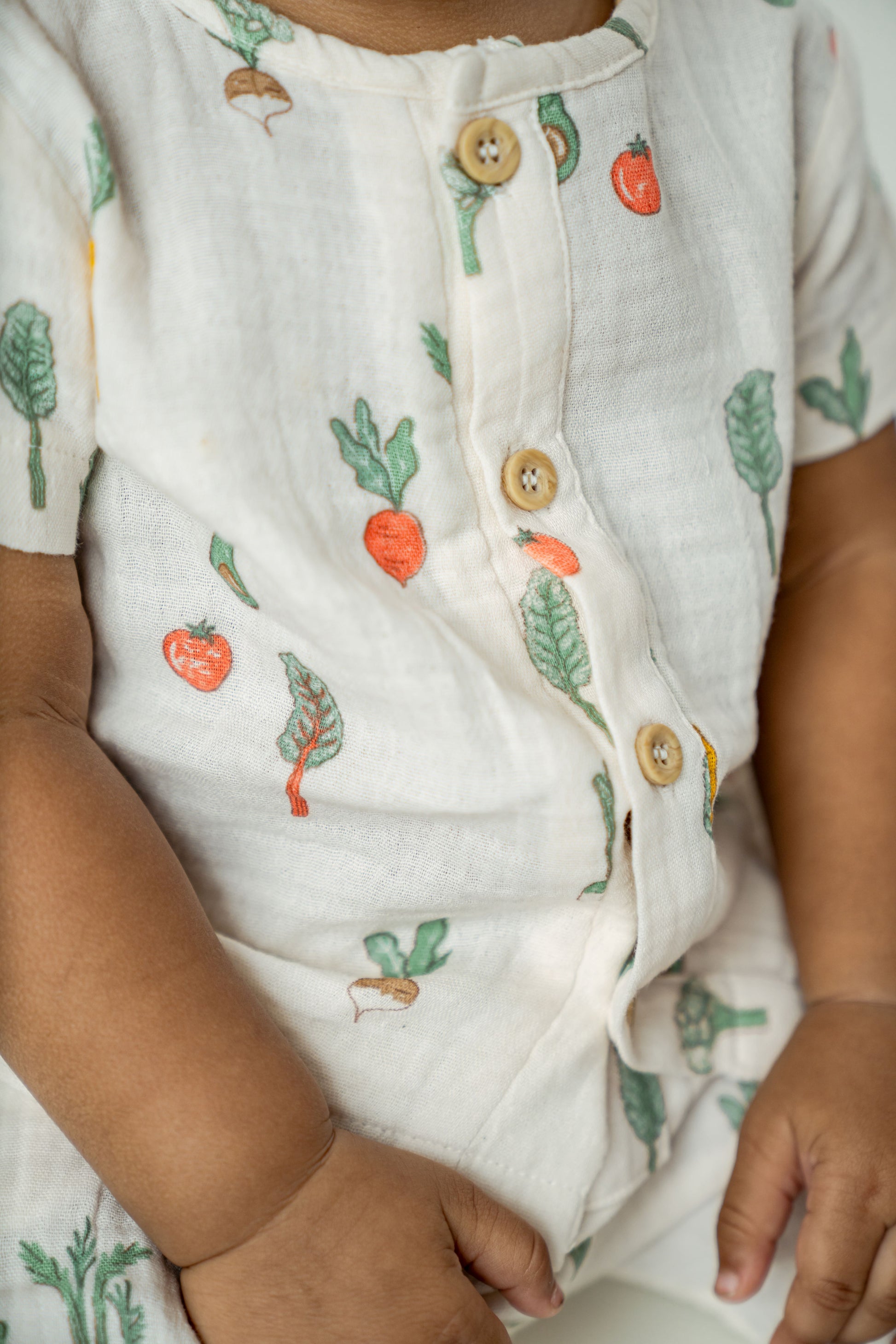 Organic cotton toddler playsuit featuring whimsical garden vegetables on a soft white background - perfect for cozy, eco-friendly everyday wear.