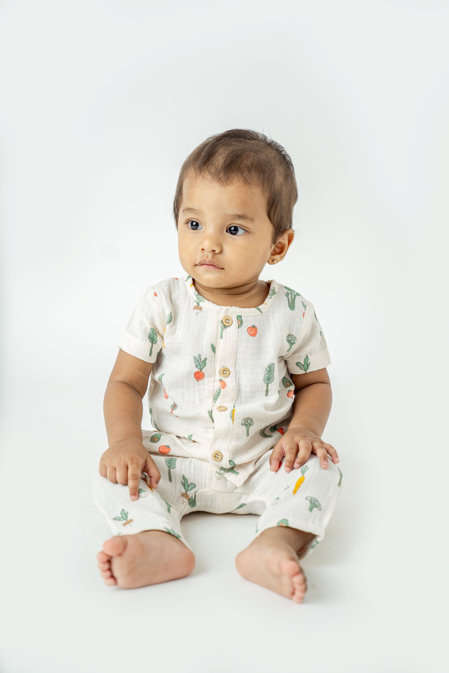 Organic cotton toddler playsuit featuring whimsical garden vegetables on a soft white background - perfect for cozy, eco-friendly everyday wear.
