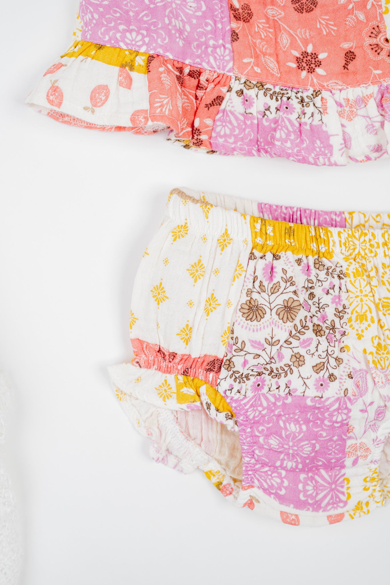 Infant organic cotton sleeveless jhabla set with colourful patchwork print in shades of pink, yellow and white, featuring floral and geometric patterns. Soft, breathable fabric designed for newborn comfort.