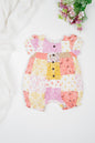 Baby romper in soft organic cotton with colourful patchwork print in pink, yellow and white tones, featuring floral and geometric patterns. Designed with snap buttons for easy dressing and diaper changes.